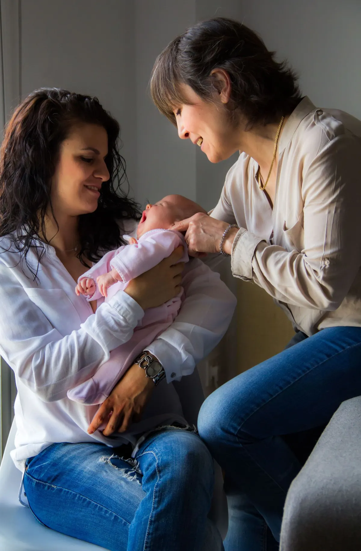 A mother and grandmother sharing a tender moment with a newborn baby at home